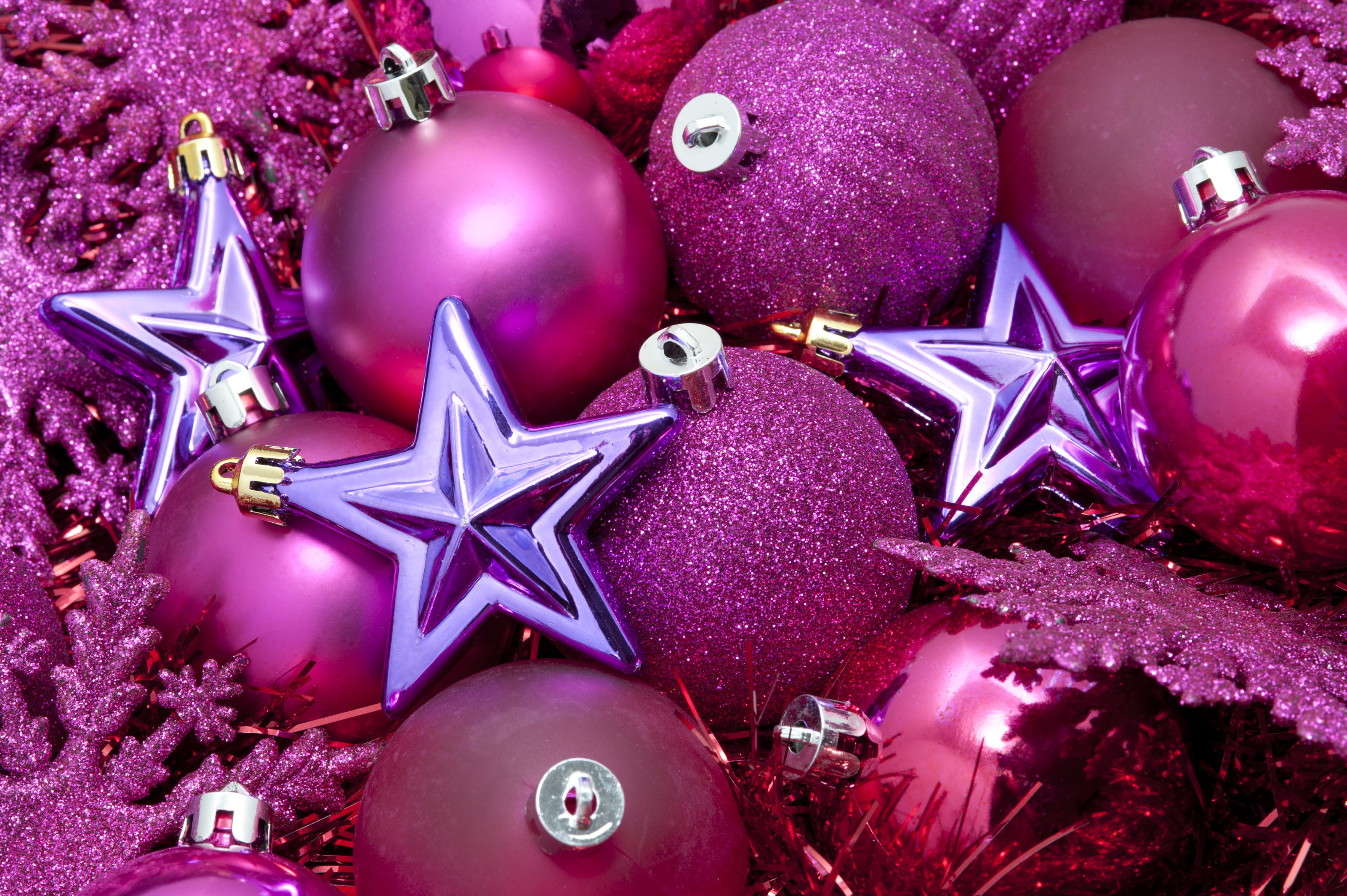 Seasonal background with a collection of pink Christmas bauble decorations  and tinsel topped with purple stars 3200x2129